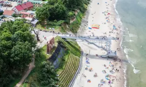 Widok na plażę z kładką i ruinami. Ludzie odpoczywają na piasku, ciesząc się atrakcjami nad morzem.