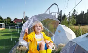 Chłopiec w żółtej kurtce i kaloszach pod przezroczystym parasolem, w tle rollercoaster. Czy Energylandia jest otwarta w deszcz?