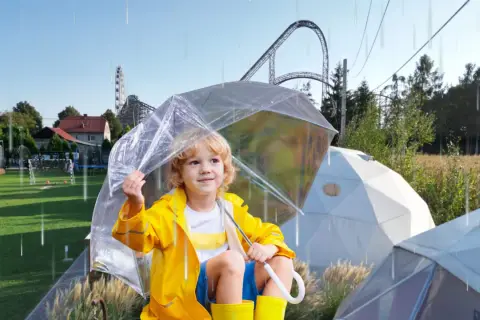 Chłopiec w żółtej kurtce i kaloszach pod przezroczystym parasolem, w tle rollercoaster. Czy Energylandia jest otwarta w deszcz?