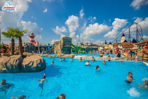 Energylandia wodne atrakcje: ludzie kąpią się w basenie, zjeżdżalnie i roller coaster w tle.