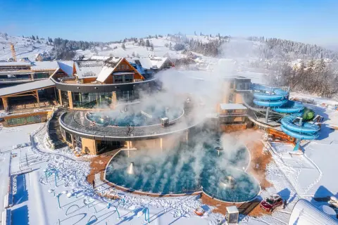 Gorący aquapark w górach, otoczony śniegiem, z parującymi basenami i niebieskimi zjeżdżalniami.
