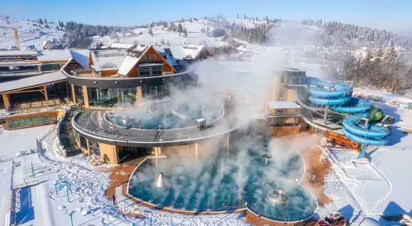 Gorący aquapark w górach, otoczony śniegiem, z parującymi basenami i niebieskimi zjeżdżalniami.