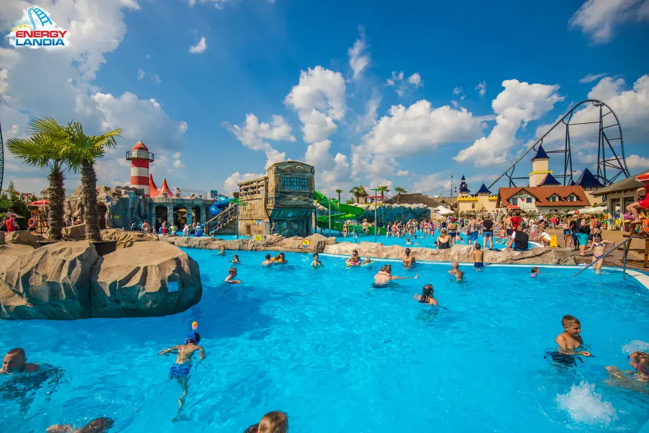 Energylandia wodne atrakcje: ludzie kąpią się w basenie, zjeżdżalnie i roller coaster w tle.