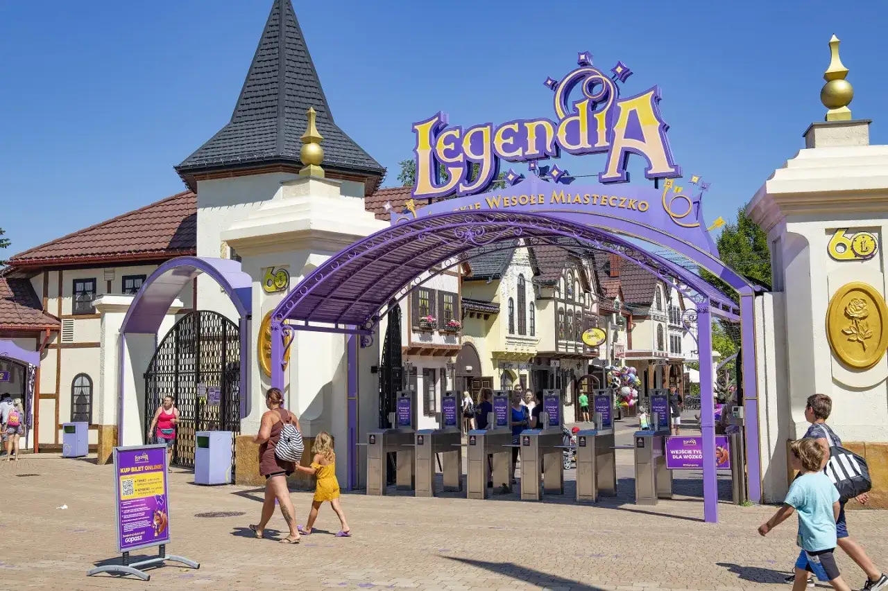 Wejście do Legendii, polskiego Disneylandu, z kolorowym napisem i bramkami. Rodziny wchodzą do parku rozrywki.