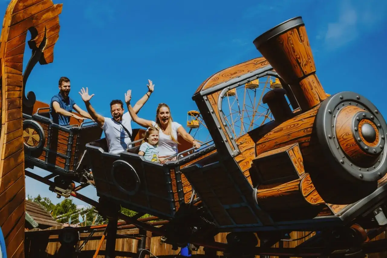 Rodzina śmieje się i macha, jadąc drewnianym pociągiem na rollercoasterze.