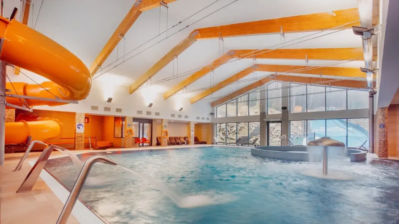 Wesoła zabawa w aquaparku hotelu w Szklarskiej Porębie: basen, zjeżdżalnie i jacuzzi pod drewnianym dachem.