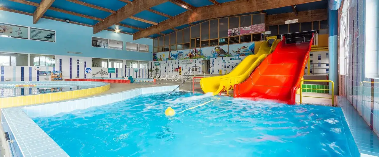 Wesoły hotel z aquaparkiem dla dzieci: basen, zjeżdżalnie żółta i czerwona, wodne atrakcje.