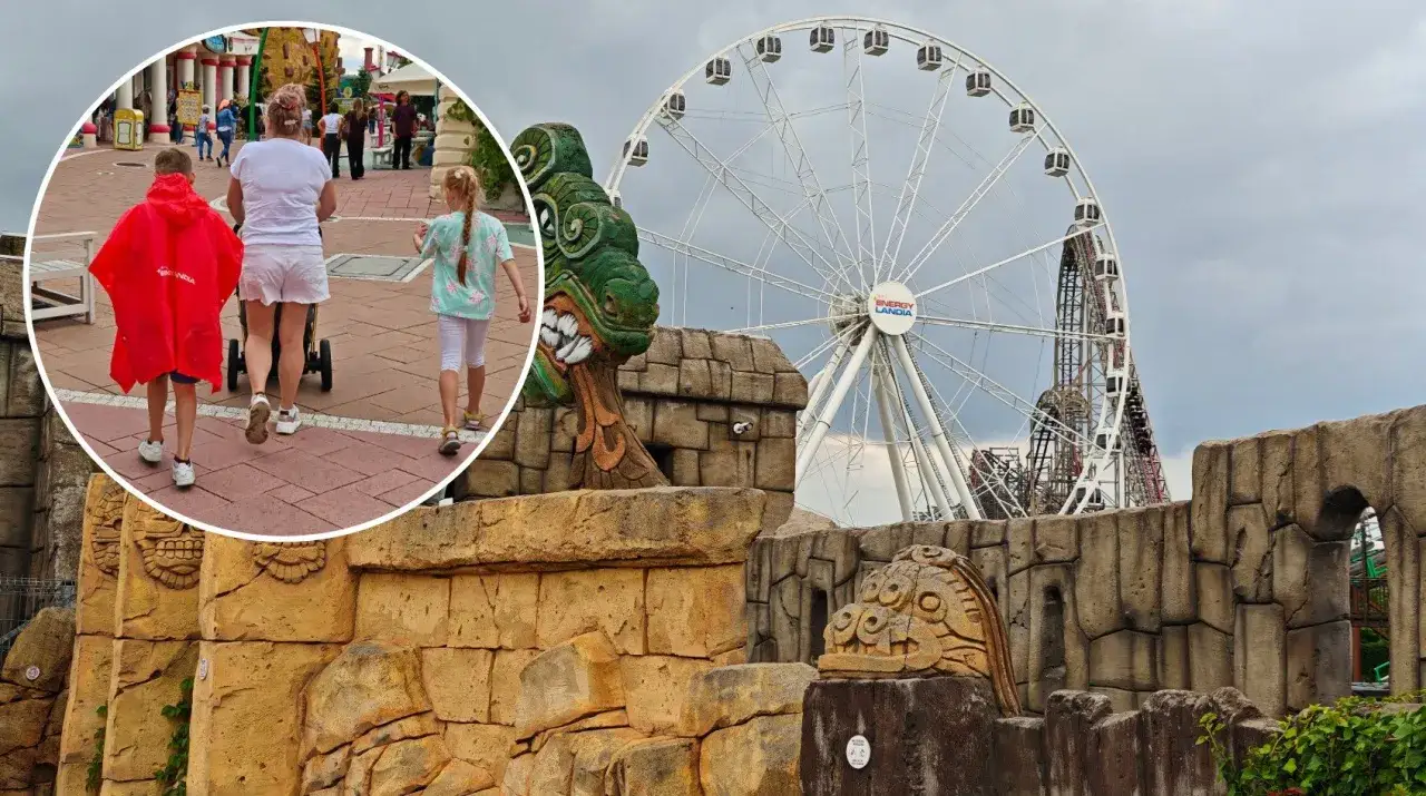Rodzina w deszczowych pelerynach spaceruje po Energylandii, gdzie widać diabelski młyn i rollercoastery. Czy Energylandia jest otwarta w deszcz? Tak!