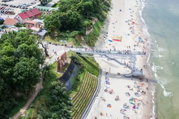 Widok na plażę z kładką i ruinami. Ludzie odpoczywają na piasku, ciesząc się atrakcjami nad morzem.